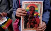 a person holding a photo of the Rainbow Madonna - an adaptation/modification of the Black Madonna image - with the halos coloured in rainbow colours of the LGBT movement