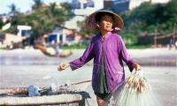 Female fisher in purple clothes on beach holding fishing nets